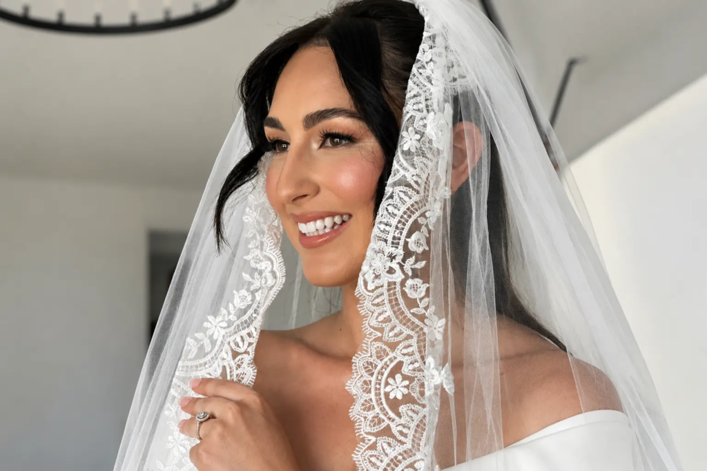 Bride wearing timeless bridal makeup with soft natural glam, radiant skin, and an elegant lace veil on her wedding day.